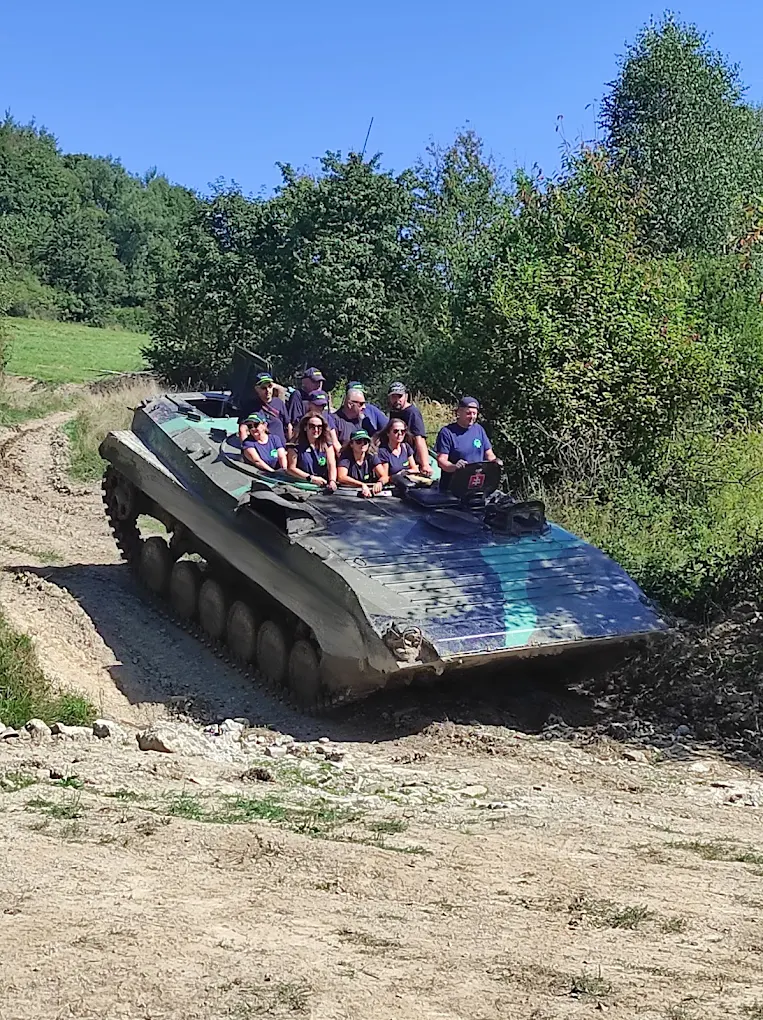 Skupina účastníkov v modrých tričkách na pásovom vozidle BVP-2 v teréne